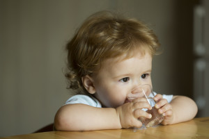 Adorable toddler drinking from a glass of water