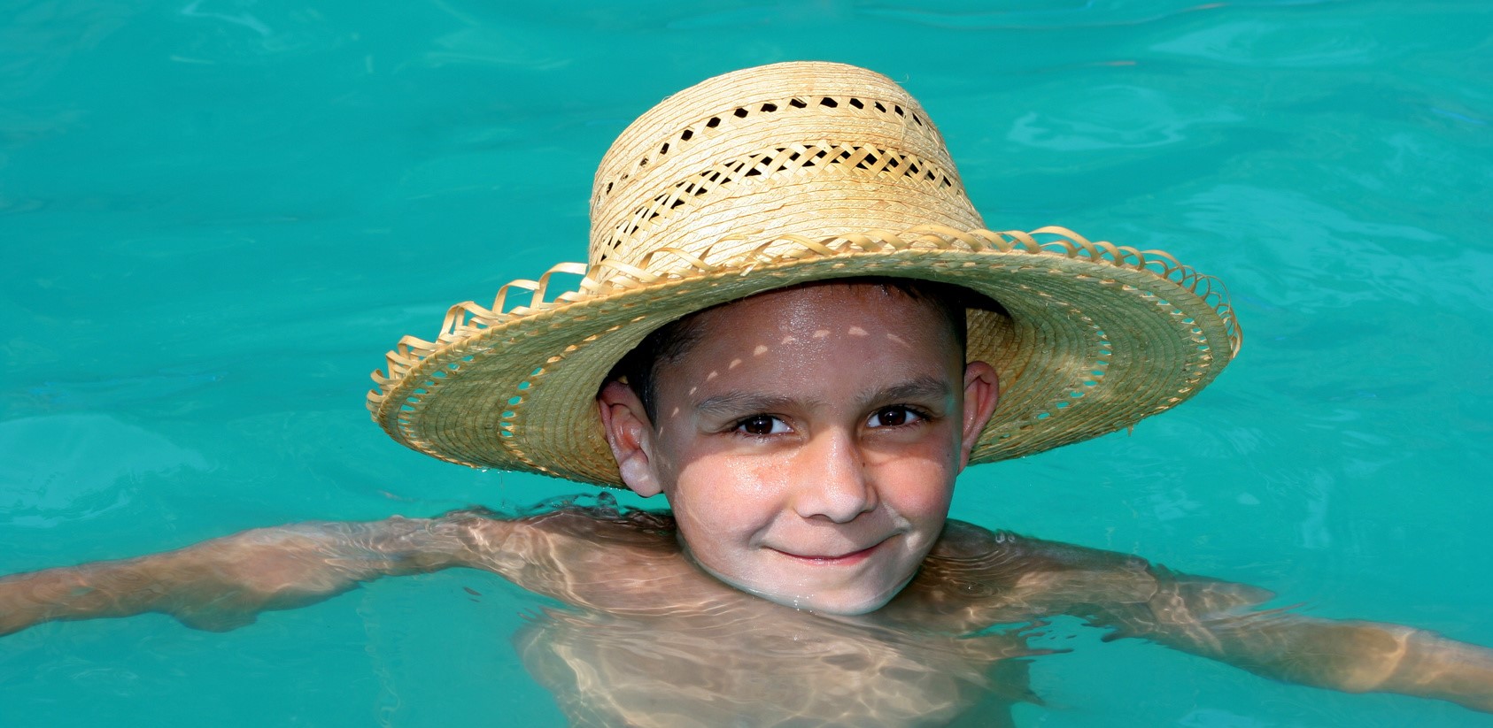 6 Ways to Stay Cool and Save Energy | Close-up of small boy with sunhat swimming in pool