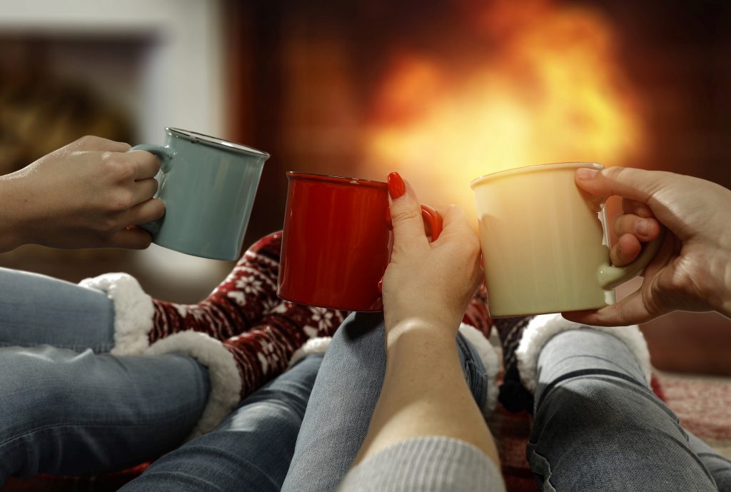 gifts that save energy and reduce waste | friends raising mugs before a fireplace | Cost Control Associates